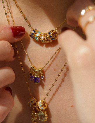 A close up of a neck and two hands wearing gold rings and chains with gemstone and gold charms