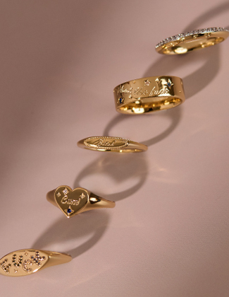 A row of assorted gold and gemstone rings on a pink background
