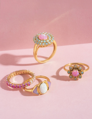 Close up of four assorted opal and gemstone gold rings on a pink background
