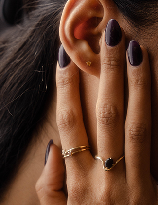 Close up of woman's ear and hand wearing assorted gemstone and gold jewelry