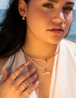 Close up of woman wearing assorted gemstone and gold jewelry with the beach visible in the background
