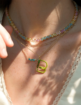 Close up image of model's neckline wearing three assorted gemstone and gold necklaces including new twisting shimmer ombre letter necklace