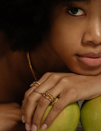 Close up of a woman wearing gold stacking rings holding a green apple
