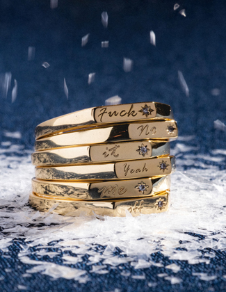 A stack of gold rings engraved with words on a snowy surface with dark blue background