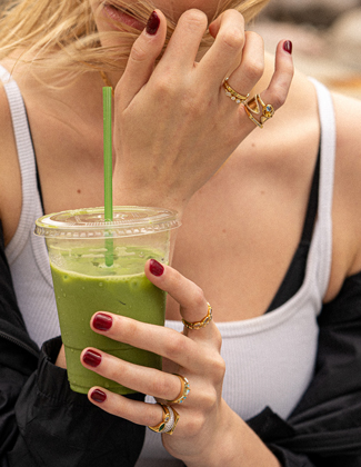 Close up of a woman wearing gold stacking rings holding a green juice