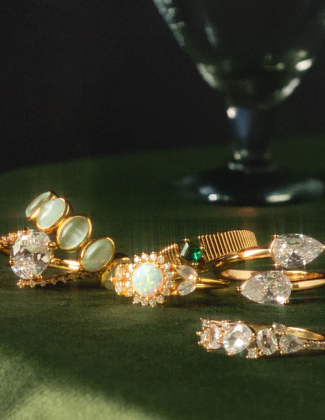 A close up of two diamond studded gold charms on gold chains laying on a dark blue background with a badge that reads 20% off