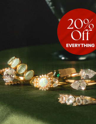 A close up of two diamond studded gold charms on gold chains laying on a dark blue background with a badge that reads 20% off