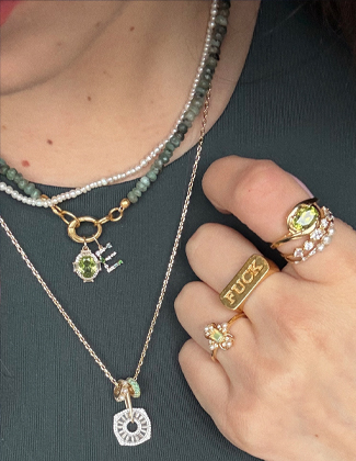 Close up of a woman wearing layered necklaces and stacking gold rings in a dark green shirt