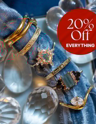Assorted gold rings on rolled up light blue velvet fabric with a badge that reads 20% off