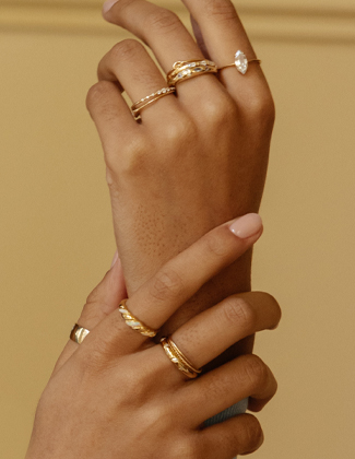 Close up image of two hands wearing various gold and gemstone rings.