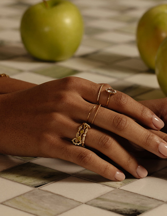 Close up of a woman wearing gold stacking rings with green apples in the background