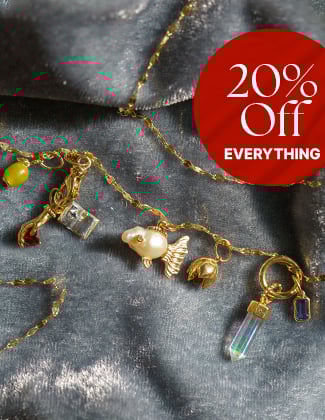 Assorted gold charms on a gold chain laying on light blue velvet fabric with a badge that reads 20% off