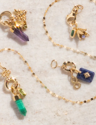 Clusters of solid gold charms and a gold chain laying over a beige stone surface