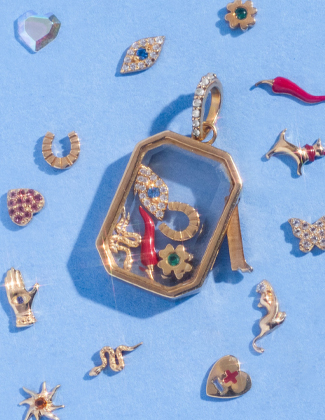 A glass charm locket with charms inside and laying around it over a blue backgorund