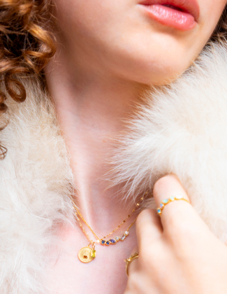 A close up of a woman wearing whote fur with three layered gold necklaces with a badge that reads 20% off