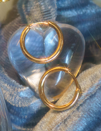 A close up of gold hoop earrings against light blue velvet with a badge that reads 20% off