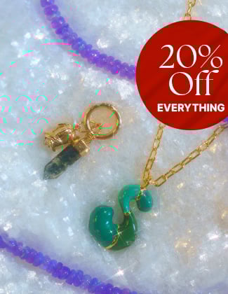 A close up of colorful necklaces and charms laying in faux snow with a badge that reads 20% off