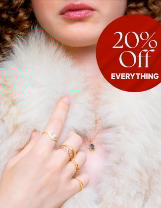 Close up of a woman wearing white fur and assorted gold rings and necklaces with a badge that reads 20% off