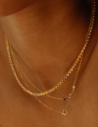 Close up image of a woman wearing stacked gold and gemstone necklaces.