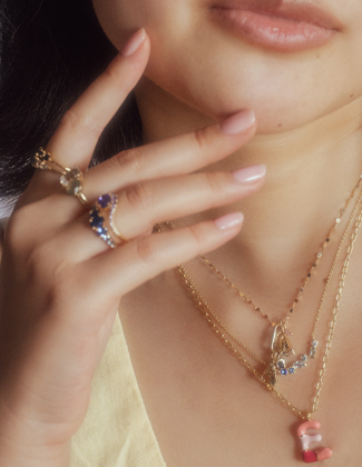 A woman wearing stacked gold rings and layered gold necklaces in a pastel yellow top