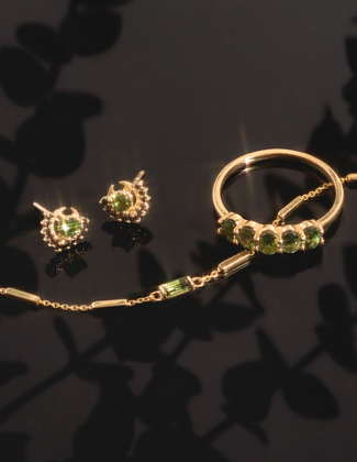Close up of gold and gemstone bracelet earrings and ring on a black background with floral detail