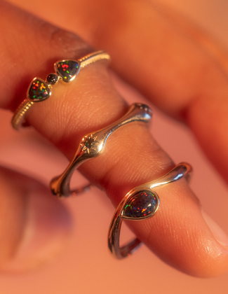 A close of up of three gold and black opal rings on a finger with a warm orange background
