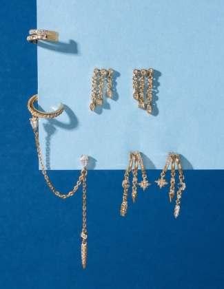 Close up of four different gold and gemstones earring styles by designer Aaria London on a blue background