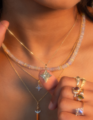 Close up image of a woman's neck and hand wearing assorted gemstone and gold necklaces and rings