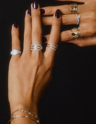 Close up of two hands wearing gold and gemstone rings on a black background