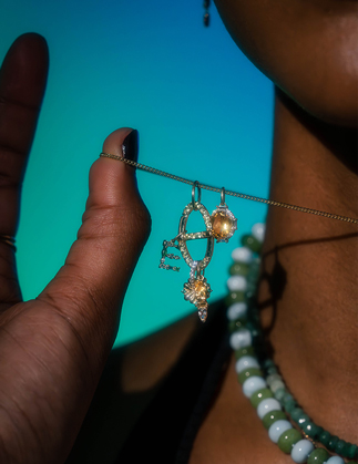 close up of person's neck and hand wearing gold and gemstone necklaces in front of blue background.