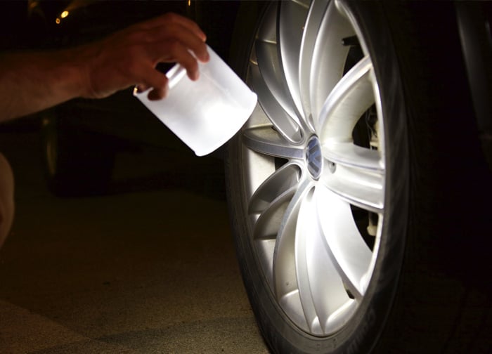 A person is inspecting a car wheel at night, using a light source to illuminate the tire and rim.