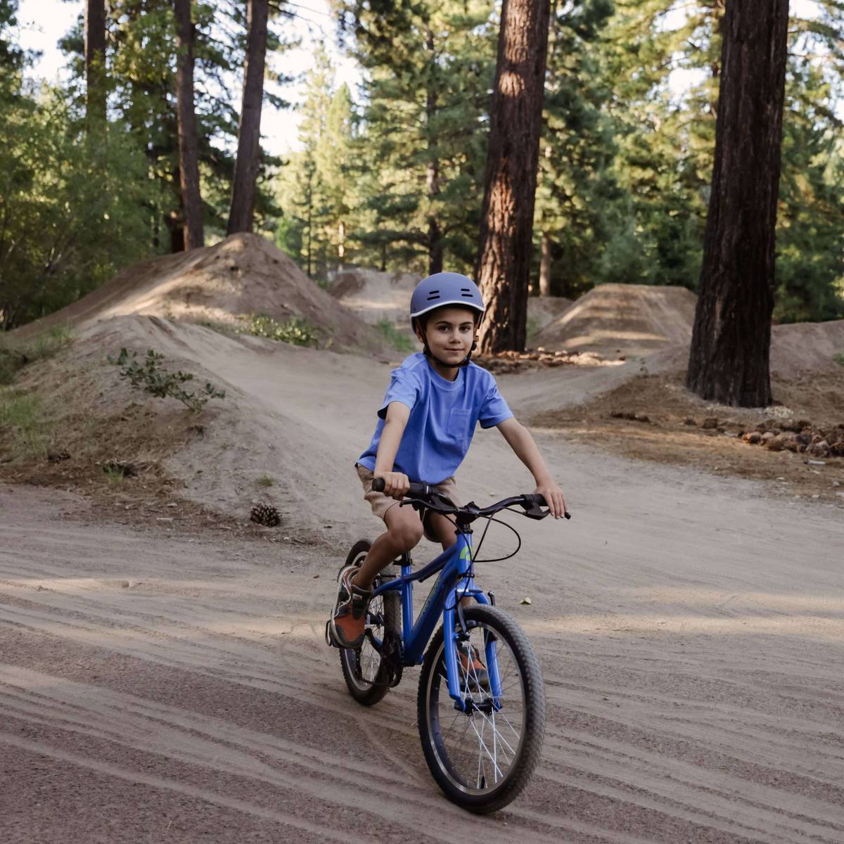 A young boy riding a blue Dart 20” Kids 7 Speed on a dirt path, enjoying the outdoors.