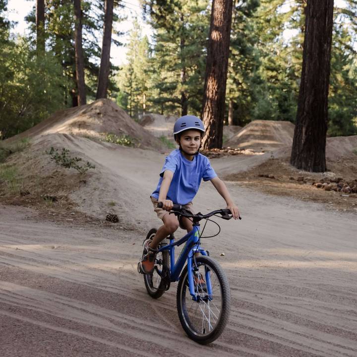 A young boy riding a blue Dart 20” Kids’ 7 Speed on a dirt path, enjoying the outdoors.