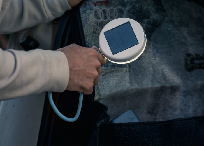 A person holds a circular device with a solar panel, inspecting a surface, possibly related to automotive or technology.