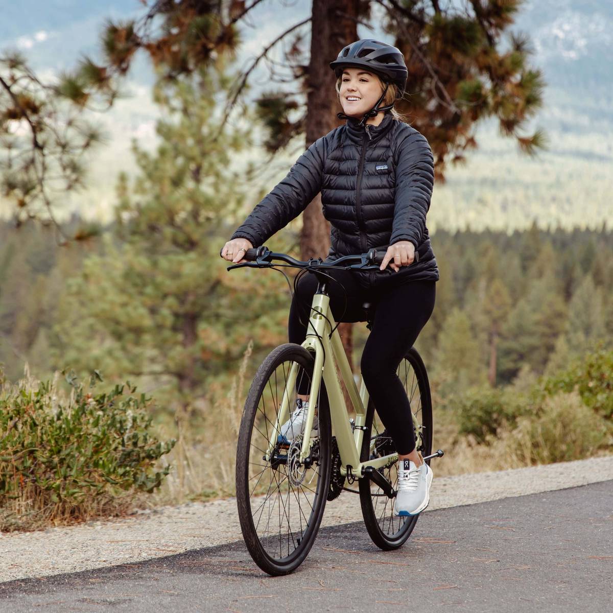 A person rides a light green bicycle on a paved pathway surrounded by greenery.