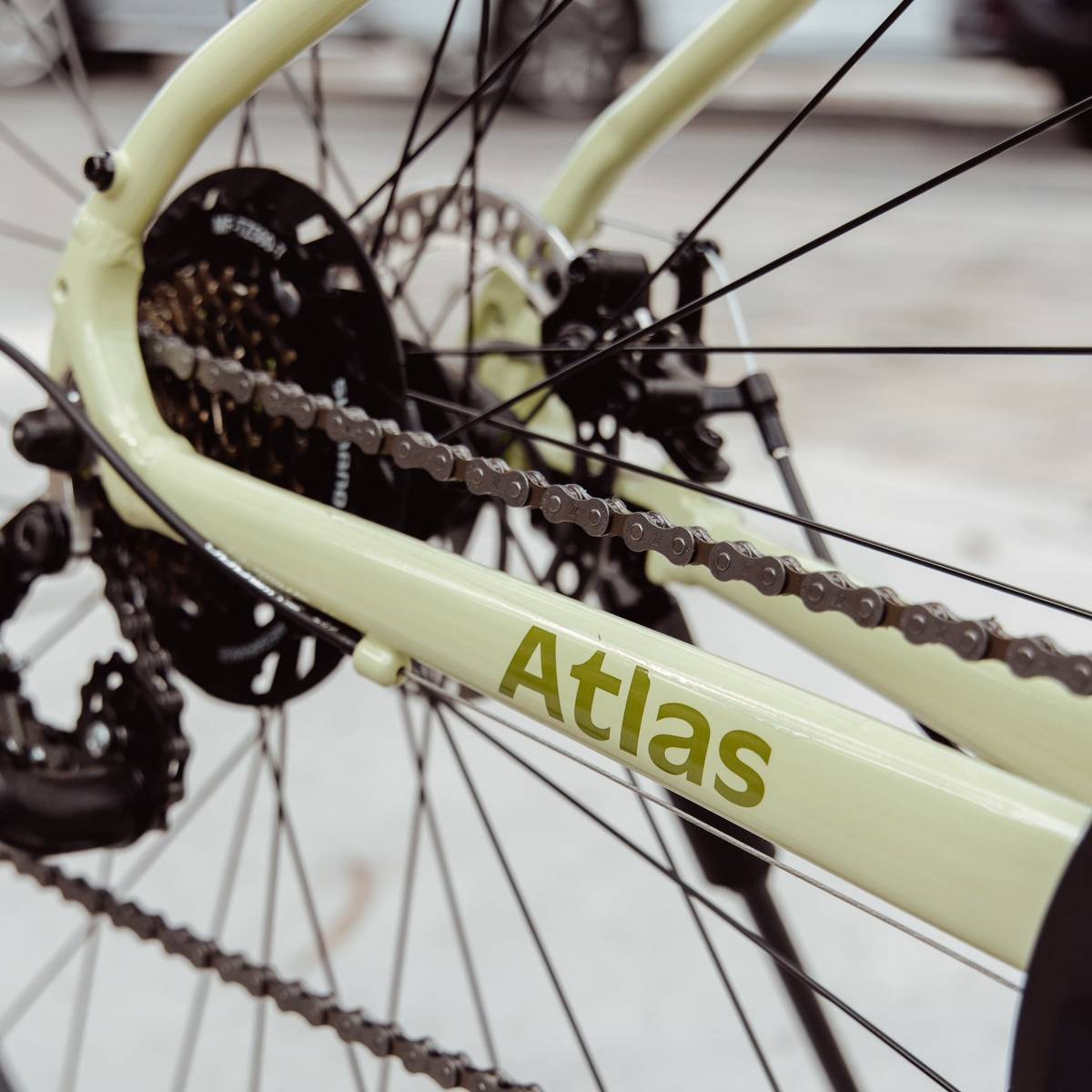 Close-up view of a pale green bike frame with the word "Atlas" prominently displayed, showcasing the chain and gears behind the rear wheel.