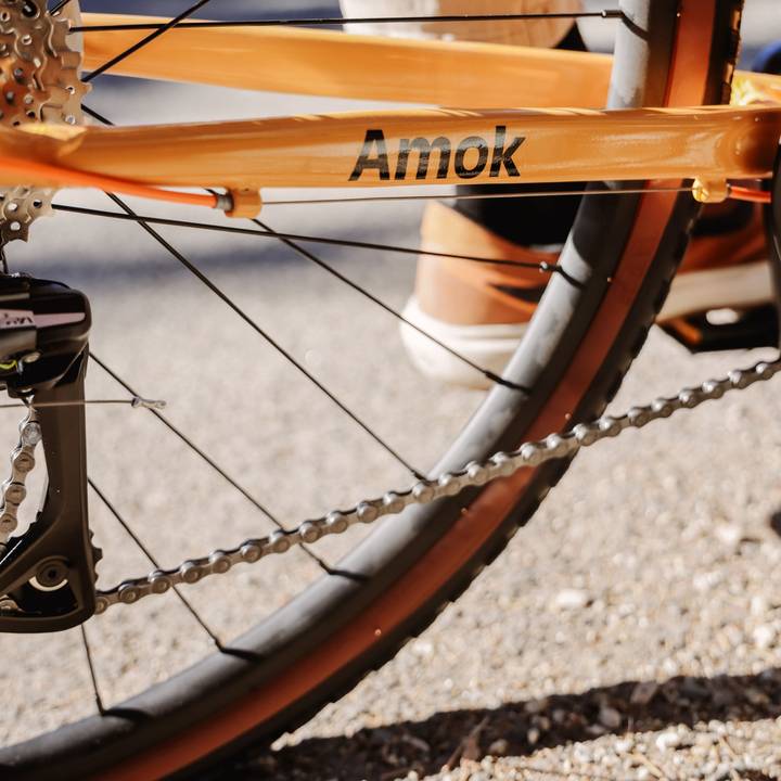 Close-up of a bicycle's rear wheel and orange frame labeled "Amok."