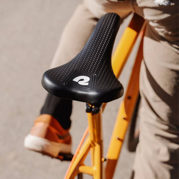 Close-up of a black bicycle seat with a retrospec logo on an orange frame.