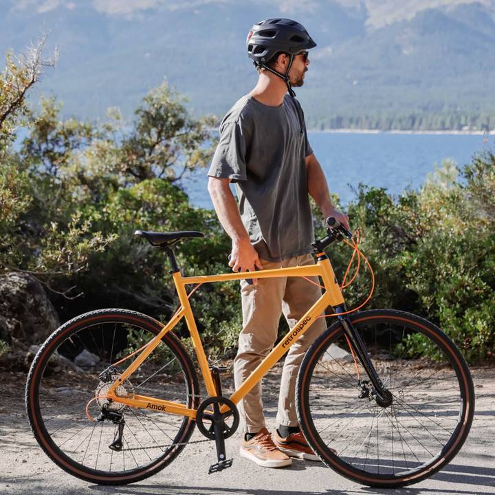 Person with a yellow bicycle on a paved path near greenery and a body of water.