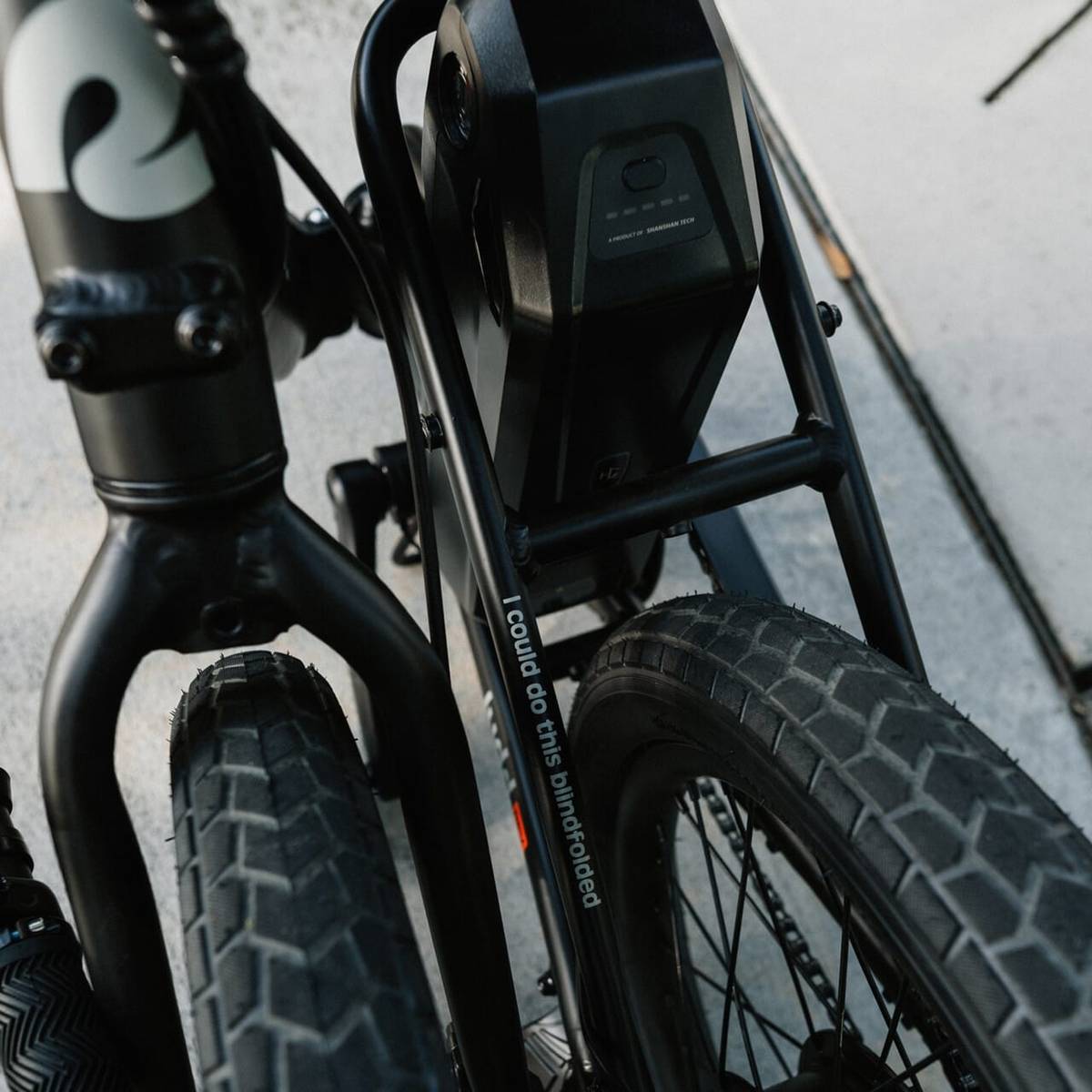 A close-up view of the Judd Rev Folding Electric Bike collapsed showcasing it's compact design while zooming in on it's frame and tires, featuring a battery and a playful slogan, "I could do this blindfolded" on the frame's side.