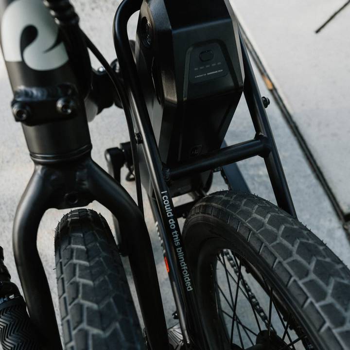 A close-up view of the Judd Rev Folding Electric Bike collapsed showcasing it's compact design while zooming in on it's frame and tires, featuring a battery and a playful slogan, "I could do this blindfolded" on the frame's side.
