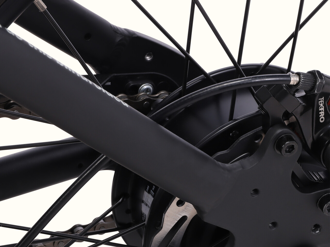 Close-up of a bicycle's rear wheel, showcasing the black frame, Tektro brake caliper, and intricate hub and chain details.