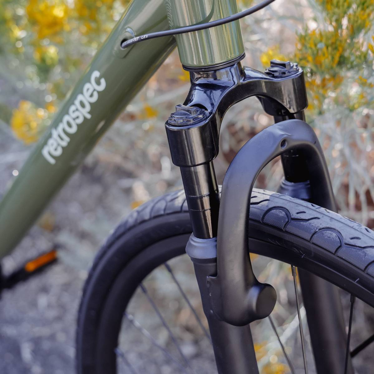 Close-up of a bicycle's front fork and wheel with an olive green frame bearing the brand name "retrospec."