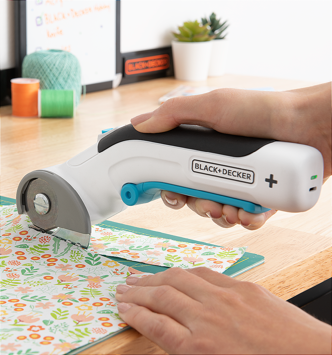 close-up of a BLACK+DECKER power rotary cutter being used to cut floral fabric