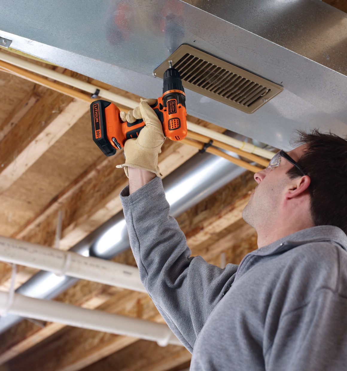 Man using drill/driver to secure a vent to an overhead air duct.