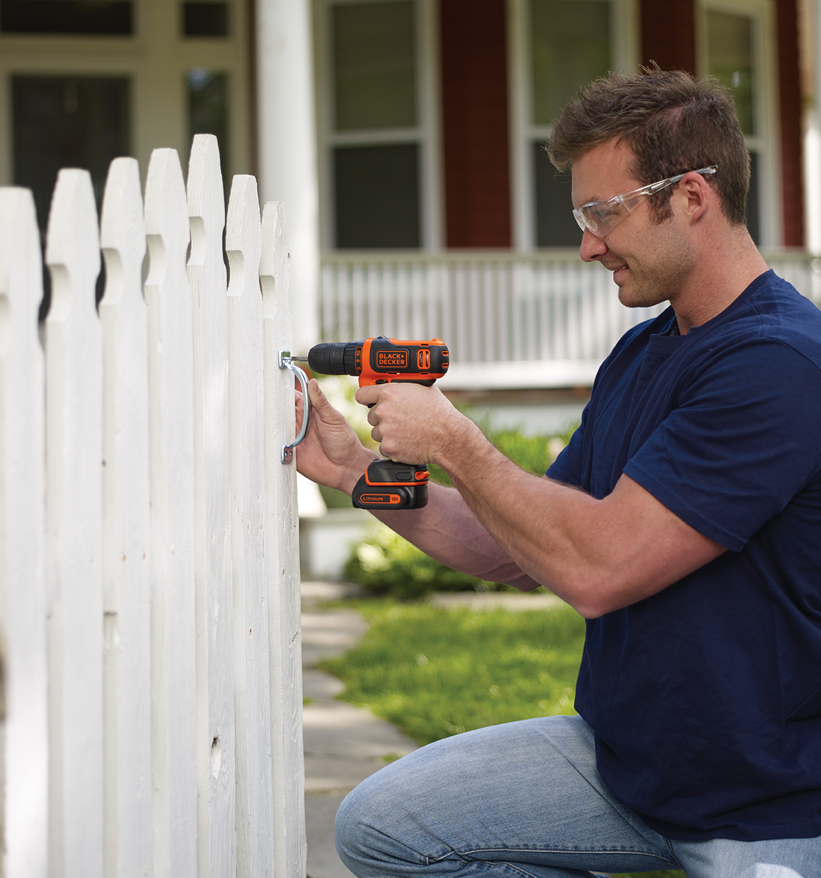 Man using a 12V Max Drill/Driver to secure a handle to a white picket fence.