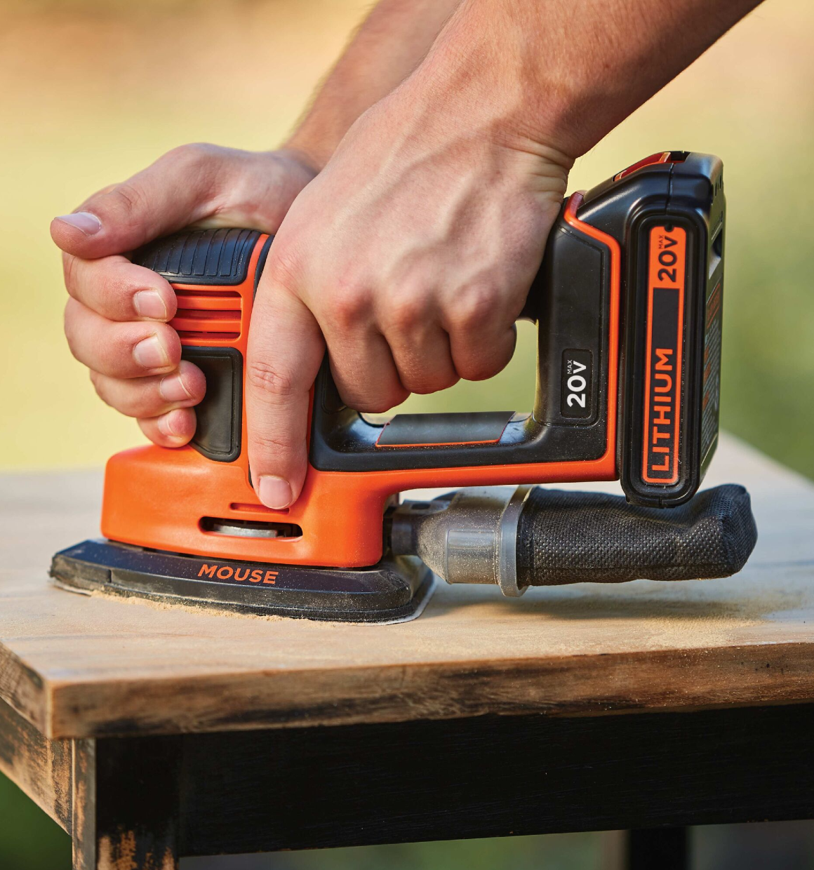 Compact and ergonomic design feature of MOUSE Cordless Sander being used by person to sand the top of a small square wooden table.