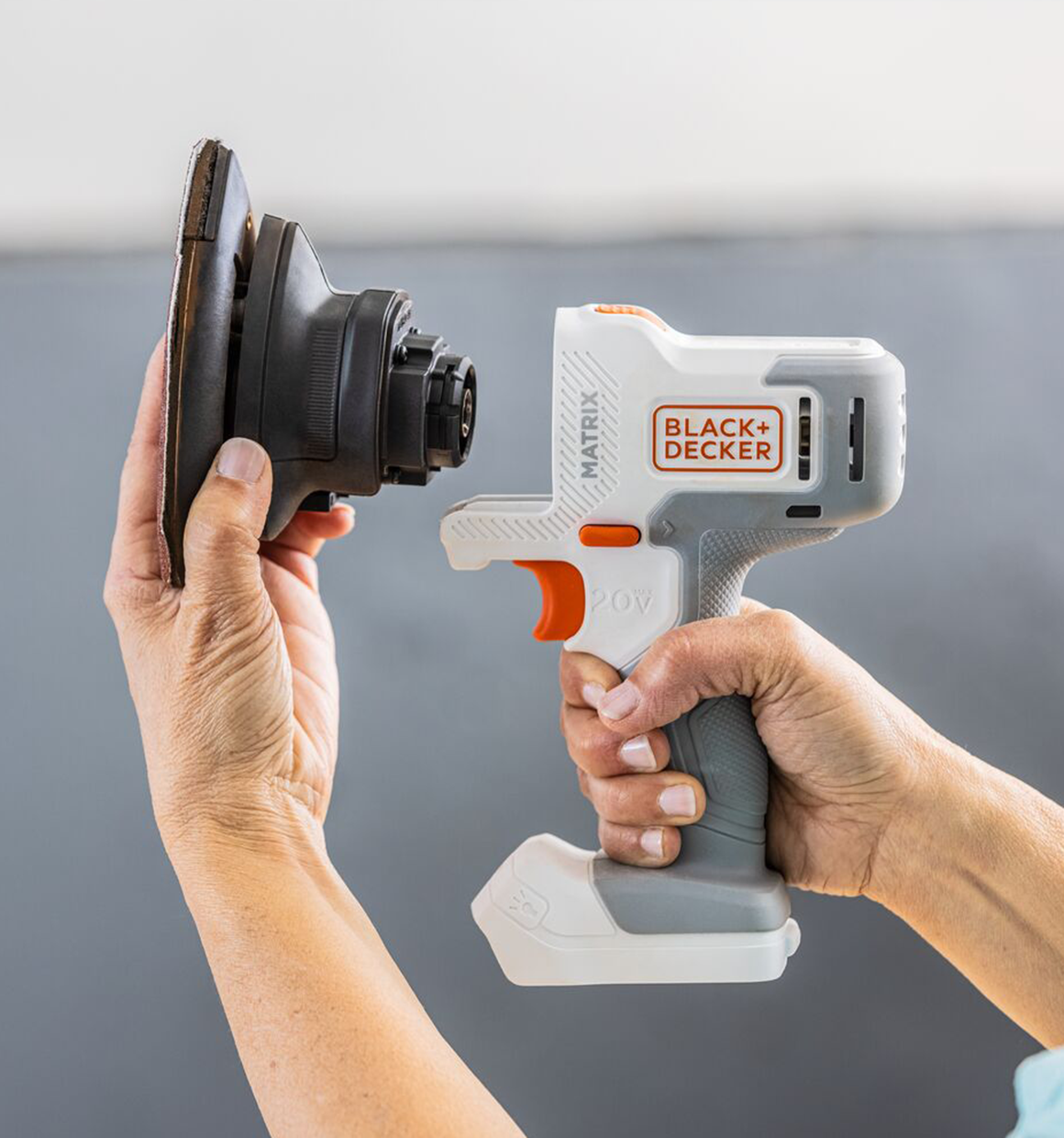 Person shows how the BLACK+DECKER MATRIX Sander attachment slides on to the orange, 20 Volt MATRIX Power Unit.