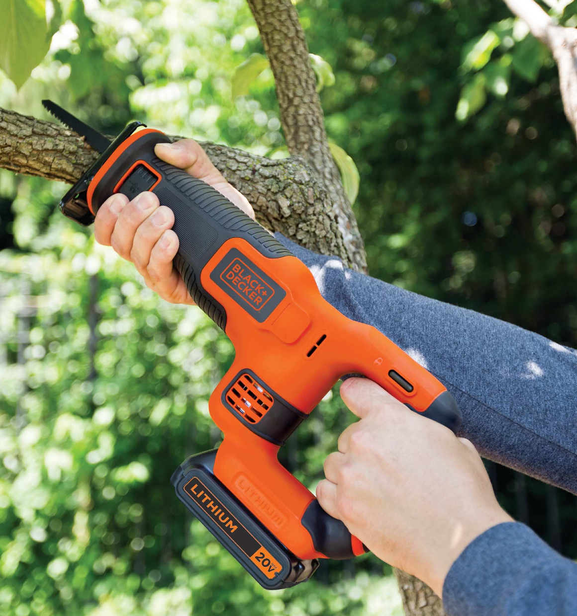 Cordless reciprocating saw being used to saw a branch.