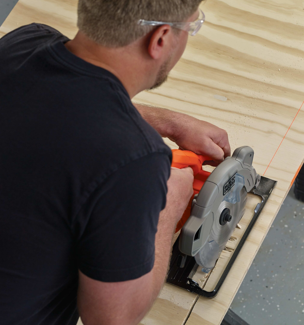 Over shoulder view of man using a 7-1/4 Inch Circular Saw with Laser to cut plywood.